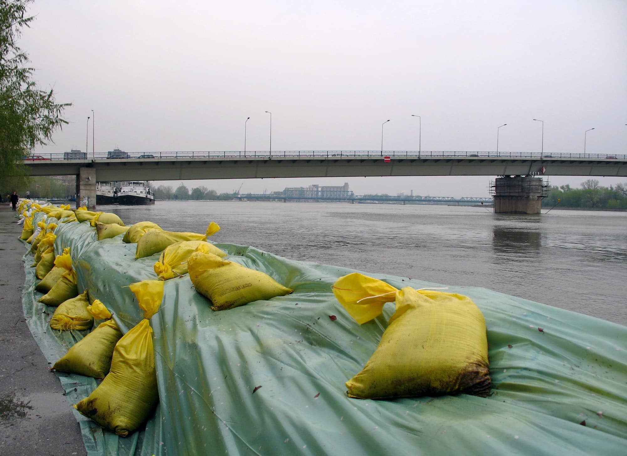 Row of large sandbags flood barricade protecting river against flooding